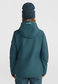 Mėlynas vandeniui atsparus džemperis su gaubtu, turi logotipą ant nugaros, elastingas rankogaliai ir lygi medžiagos tekstūra. Papildytas tamsiu kepurėliu.