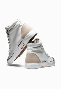 Zapatillas altas con una parte superior de cuero blanco, detalles en gamuza beige y una suela de goma. Presenta un logotipo negro y rojo cerca del talón.
