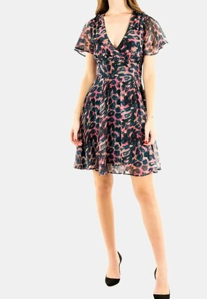 Kobieta w sukience do kolan z krótkim rękawem i dekoltem w serek, ozdobionej różowo-czarnym wzorem panterki, w połączeniu z czarnymi szpilkami na białym tle.