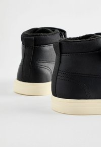 Bottines noires en matériau synthétique texturé avec des semelles de couleur crème. Comprend un col rembourré et des côtés élastiques pour un enfilage facile.
