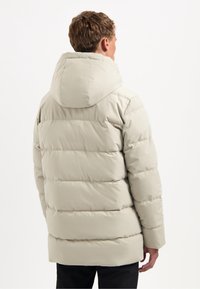 Lichtbeige gewatteerde jas met een capuchon, voorzien van horizontale gestepte delen en een iets langere achterkant. Soepele, geïsoleerde stof.