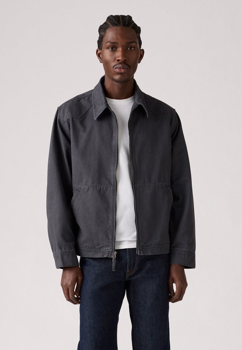 Graue, mit Reißverschluss geschlossene Jacke mit spitzem Kragen und seitlichen Taschen. Hergestellt aus einem strapazierfähigen Material mit glatter Textur und legerer Passform.