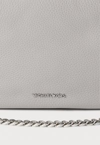 Γκρι δερμάτινη τσάντα χειρός με υφή στην επιφάνεια, ασημένια αλυσίδα για λουρί και ανάγλυφο το όνομα της μάρκας "MICHAEL KORS" στο μπροστινό μέρος.