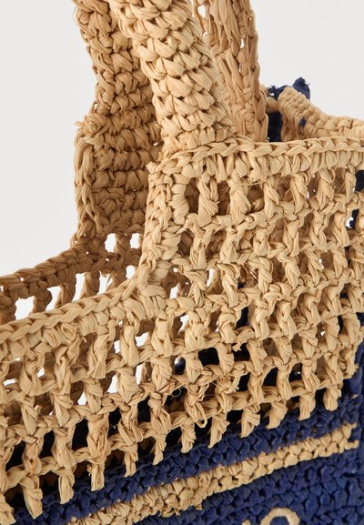 Gros plan d'un sac en paille tressée beige et marine avec des anses épaisses tressées et un motif de tissage ouvert et texturé.