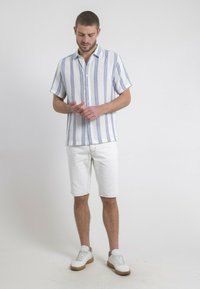 Chemise à manches courtes avec des rayures bleues et blanches ; shorts blancs ; baskets blanches avec semelles brunes ; design minimaliste.