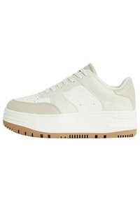 Bílé kožené tenisky s texturovanou béžovou špičkou a silnou, hnědou gumovou podrážkou s výřezy. Viditelné tkaničky a prošité detaily.