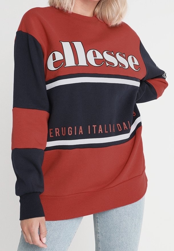 Czerwony i granatowy sweatshirt z białymi paskami, z logo "ellesse" na piersi. Wykonany z miękkiego materiału o luźnym kroju.