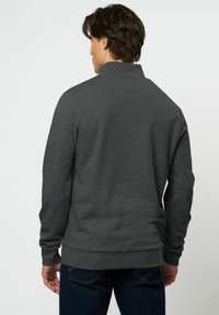 Pulover gri închis cu guler înalt, mâneci lungi și manșete și tiv striate. Fabricat din material neted și moale. Pare ajustat la talie.