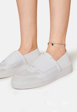 Weiße Slipsneaker aus einer Mischung aus glatten und strukturierten Materialien. Sie verfügen über eine weiche Wildlederfront, eine dicke Sohle und ein Logo am Riemen.