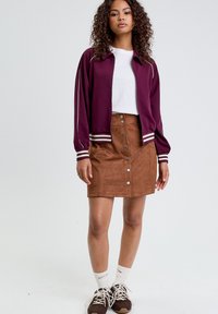 Bordeaux zip-up bomberjakke med hvide striber, parret med en brun ruskinds knap-ned nederdel. Stylet med hvide sokker og brune sneakers.