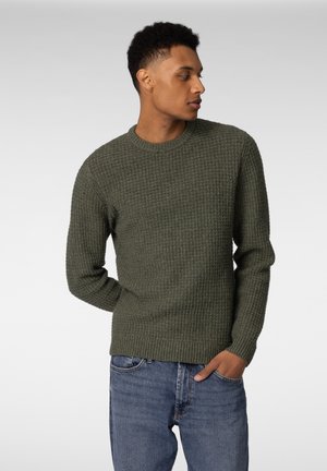 Strikkegenser i olivengrønn med teksturert mønster, rund hals, og lange ermer, kombinert med blå jeans.