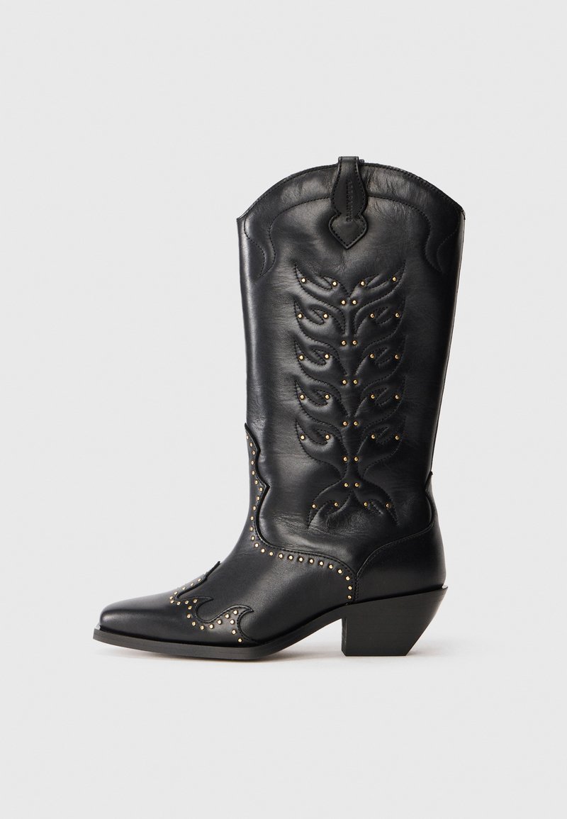 Botas de cowboy de cuero negro con punta afilada, costuras decorativas y tachuelas en tono dorado a lo largo de la suela. Tacón bajo y cuadrado.