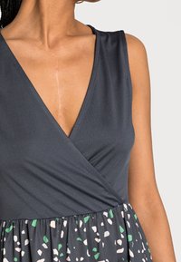 Czarna szara sukienka kopertowa z dekoltem w serek, teksturowanym bodicem oraz wzorzystą spódnicą z pastelowymi akcentami w odcieniach zieleni i różu.