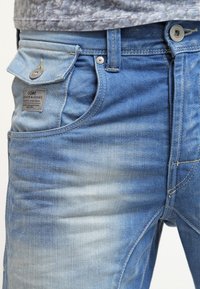 Vaaleansiniset farkut sisältävät haalistuneen pesun, perinteisen viidennen taskun muotoilun, metalliset varusteet ja merkin takataskussa.