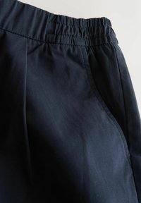 Marineblaue Hose mit elastischem Bund aus weichem Stoff, mit Falten und Seitentaschen für zusätzlichen Komfort und praktische Nutzung.