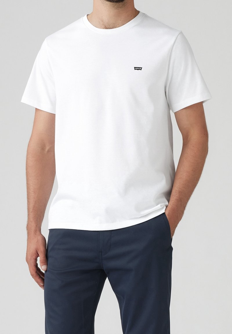 T-shirt en coton blanc avec des manches courtes, un décolleté rond et un petit logo Levi's noir sur la poitrine ; associé à un pantalon bleu marine.