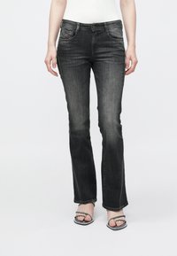 Μαύρο τζιν καμπάνα με διακριτικό ξέβαμμα, πέντε τσέπες και κλείσιμο με κουμπί. Φορεμένο με σανδάλια με ασημένιες λεπτομέρειες.