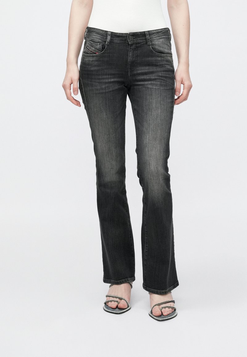 Μαύρο τζιν καμπάνα με διακριτικό ξέβαμμα, πέντε τσέπες και κλείσιμο με κουμπί. Φορεμένο με σανδάλια με ασημένιες λεπτομέρειες.