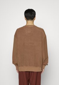 Sudadera marrón de corte oversize, con puños y dobladillo acanalados, textura suave, escote redondo y detalles de costura sutiles en la parte trasera.