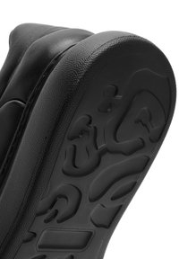 Suela de zapatilla negra con detalle de patrón texturizado, material de goma suave y diseño de borde redondeado. La banda de rodadura indica funcionalidad de agarre.