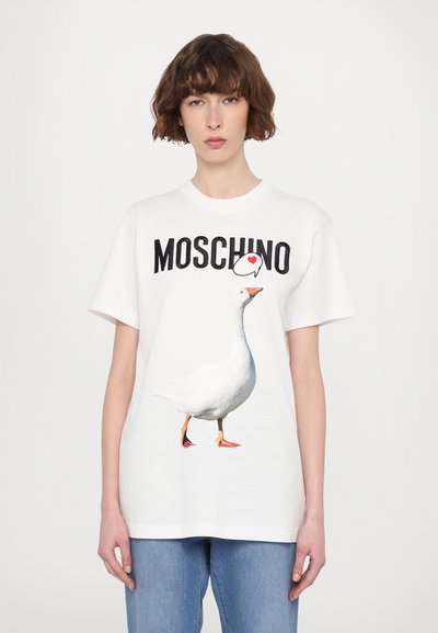 Bijela pamučna majica s velikim grafičkim prikazom guske u hodu i riječi "MOSCHINO" u crnoj boji iznad. Ležeran dizajn, kratki rukavi.