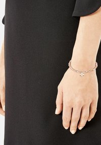 Braccialetto d'argento con perline rosa e un piccolo ciondolo a forma di fiore, indossato su una mano, su uno sfondo nero semplice.