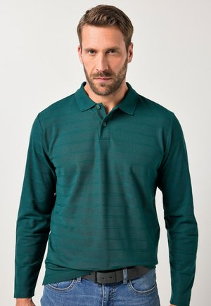 Polo a maniche lunghe di colore verde scuro con colletto, caratterizzato da un sottile motivo a righe tono su tono e una chiusura con due bottoni. Indossato con jeans blu.