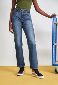 Hoge taille blauwe denim jeans met een rechte pijp, met subtiele stiksels en gecombineerd met zwart en oranje high-top sneakers.