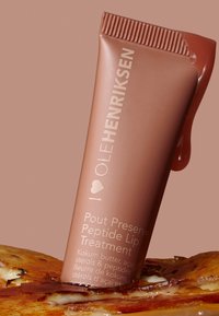 Tube von Ole Henriksen Pout Preserve Peptide Lip Treatment mit Lippenbalsamprobe und glänzendem braunem Hintergrund.