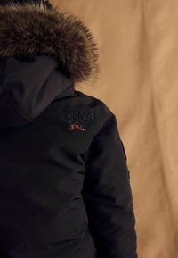 Čierna prešívaná bunda s umelou kožušinou na kapucni. Obsahuje červený a čierny vyšitý logo "SUPER DRY JPN." na ľavej strane hrude.