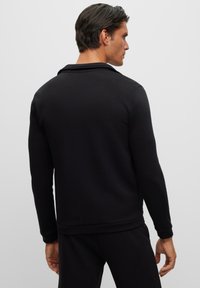 Svart sweatshirt med lång ärm och krage. Slät tygkvalitet, strukturerad passform och ribbade muddar och nertill. Minimalistisk design utan synliga mönster.