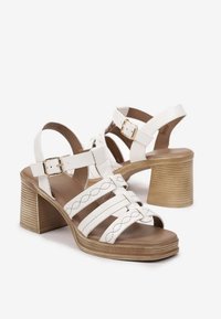 Sandales à talons blancs avec plusieurs brides, un bout carré et un talon épais texturé. Détail de boucle ajustable en métal doré.