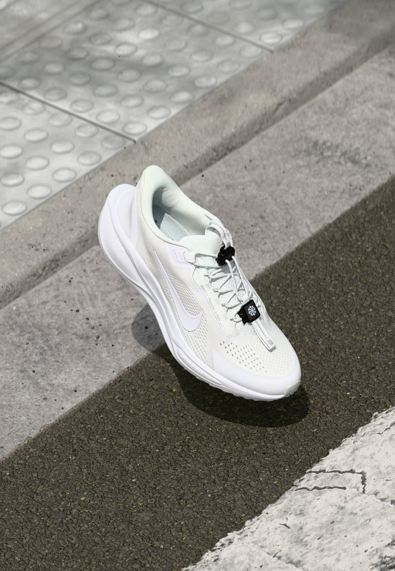 White athletic shoe made of mesh and rubber, features a rounded shape, textured surface, and a black accent with a toggle lace system.