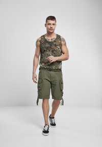 Camo tank top földszínekben, olíva zöld cargo rövidnadrággal, amely oldalzsebekkel van ellátva, és fekete sportcipő fehér fűzővel.