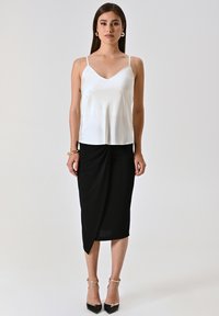 Witte satijnen camisole met dunne bandjes, gecombineerd met een zwart gekleed knie-lengte rok met een gewikkeld ontwerp. Zwarte hoge hakken.