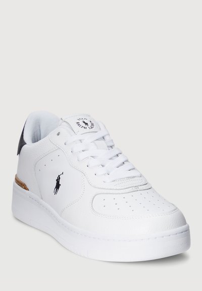 Hvit lær sneakers med perforeringer og snøring. Har en svart detalj ved hælen samt en logo på siden og tungen.