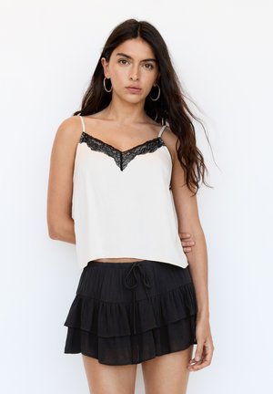 Un débardeur en crème avec des bordures en dentelle noire et des bretelles fines, associé à une mini-jupe noire à volants avec une taille à cordon.