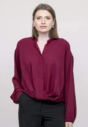 Chemise boutonnière bordeaux avec un col mandarin, manches longues, tissu texturé et coupe décontractée, assortie à un pantalon noir.