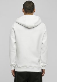Sudadera blanca con capucha espaciosa, con puños y dobladillo acanalados. Textura suave, diseño minimalista, sin logotipos ni patrones visibles.