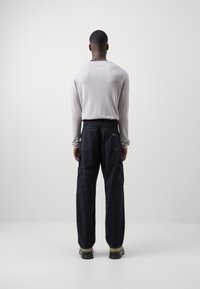 Długi rękaw jasnoszarej koszuli z okrągłym dekoltem zestawionej z ciemnoniebieskimi spodniami typu cargo z wieloma kieszeniami i kontrastującymi przeszyciami.