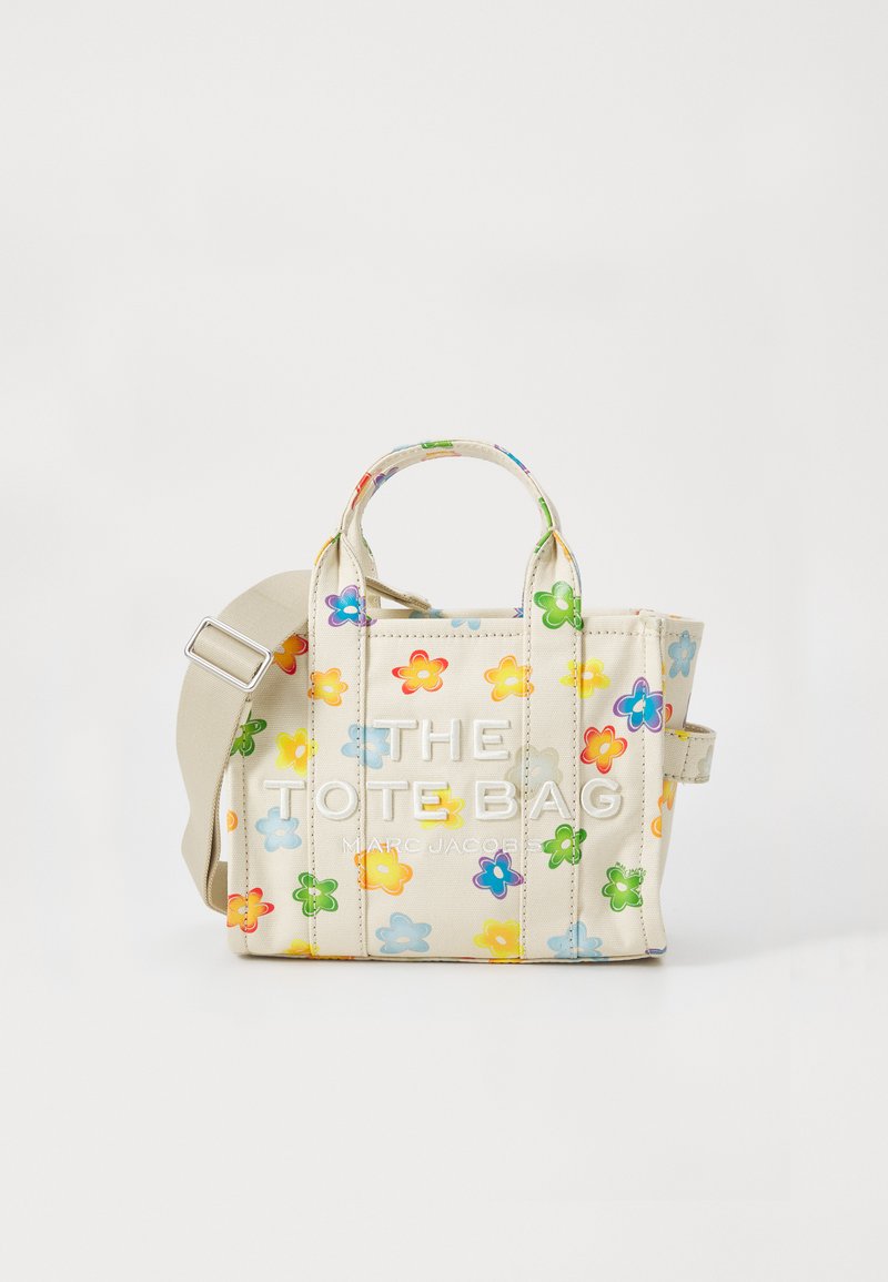 Liten beige tote veske med fargerik blomstermønster, to håndtak, justerbar skulderrem, og "THE TOTE BAG MARC JACOBS" tekst foran.