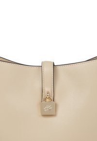 Beige bőrtáska sima felülettel, arany lakattal ellátva, elegáns, lekerekített formával.