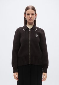 Pull marron en maille avec texture côtelée, fermeture éclair à l'avant, col et écusson logo rayé. Manches longues et bandeau à la taille en maille côtelée contrastante.