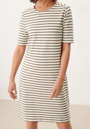 Nainen, jolla on polvenmittainen, lyhythihainen mekko, jossa on beige-valkoiset vaakaraidat, yksiväristä taustaa vasten.