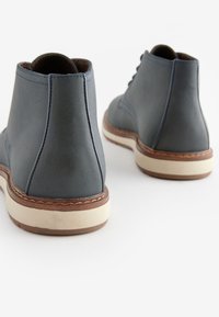 Gray leather ankle boots with a smooth texture, white rubber sole, and decorative brown stitching. Features rounded toe and lace-up design.