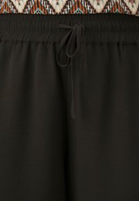 Černé lounge kalhoty s texturovaným povrchem, mají elastický pas a nastavitelné šňůrky pro přizpůsobení. Minimalistický design bez ozdob.