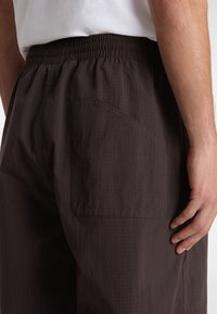 Dark brown pants made of lightweight fabric, featuring an elastic waistband, side pocket, and subtle texture.