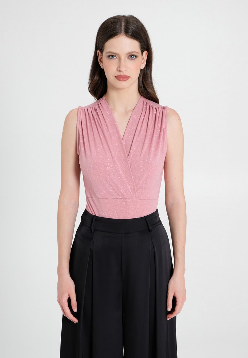 Top senza maniche rosa chiaro con design a portafoglio, caratterizzato da un sottile luccichio. Abbinato a pantaloni neri a vita alta e a gamba larga.