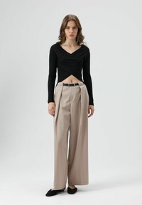 Zwart geribd longsleeve top met V-hals en cropped ontwerp, gecombineerd met beige geplooide wijde pijpen broek en zwarte instapschoenen.