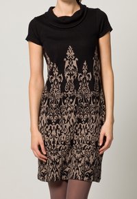 Zwarte jurk met korte mouwen en een watervalhals, met een beige versierd patroon over de onderste helft. Glad materiaal met een zachte structuur.